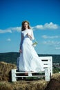 Woman bride in wedding dress on wooden bench. Sensual woman in wreath on long blond hair. Albino girl with flowers Royalty Free Stock Photo