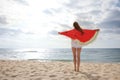 Woman with bright beach towel on sunlit seashore, back view