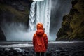 A woman in a bright colorful jacket stands and looks at a waterfall in Skogafoss, Iceland. Generative ai Royalty Free Stock Photo