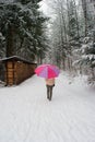 Woman with bright colorful umbrella walking alone on a snowy forest pathway seen from behind unrecognizable