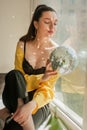 woman with bright colorfull spice makeup and Mirror disco ball with shines on shes body near window