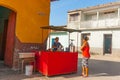 Woman in bright orange top approaches street food vendor mixing in pot