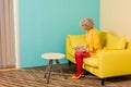 woman in bright retro clothing with golden fish in aquarium resting on sofa at colorful apartment doll Royalty Free Stock Photo