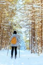 Woman with a bright yellow backpack skiing along a snowy path in the forest.