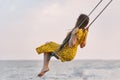 Woman in bright yellow dress rides on swing against the sea background. Alone with thoughts. Loneliness