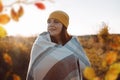 Woman in a bright yellow knitted hat wrapped in blanket in autumn nature field at sunset Royalty Free Stock Photo