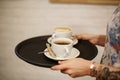 Woman bring two white cups of latte and americano coffe on tray