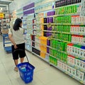 Woman bringing a blue shopping basket looking for shampoo in supermarket rack