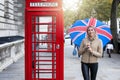 A woman with a british flag umbrella in her hand stands in front of a traditional, red telephone booth in London Royalty Free Stock Photo