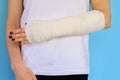 Woman with broken arm bone in cast, plastered hand on blue background. Royalty Free Stock Photo