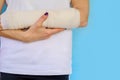 Woman with broken arm bone in cast, plastered hand on blue background. Royalty Free Stock Photo