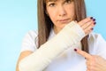 Woman with broken arm bone in cast, plastered hand on blue background. Royalty Free Stock Photo