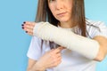 Woman with broken arm bone in cast, plastered hand on blue background. Royalty Free Stock Photo