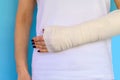 Woman with broken arm bone in cast, plastered hand on blue background. Royalty Free Stock Photo