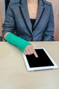 Woman with broken hand and green cast working on tablet computer in office