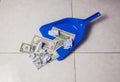 Woman broom sweeps dollars in garbage scoop on floor background