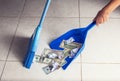 Woman broom sweeps dollars in garbage scoop on floor background