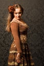 Woman in a brown dress standing beside a wall.