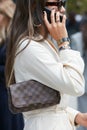 Woman with brown Louis Vuitton checkered bag, white dress and Dior bracelets before Sportmax