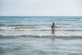 Woman bruenette with long hair in blue bikini walking in the sea water with waves. Side view.