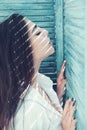 Woman brunette chilling while stands near jalousie, stripes of sunlight and shadow on her face. Heat concept. Lady wears