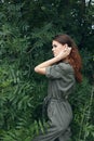 Woman Brushes hair from her face in a green jumpsuit outdoors trees Royalty Free Stock Photo