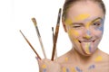 Woman with brushes and paint on face shows tongue