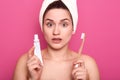 Woman brushing her teeth with shocked facial expression, girl with toothbrush on pink studio background, lady with white