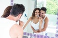 Woman brushing teeth while husband embracing her in bathroom