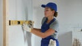 Woman builder in blue overalls measures deviations from a given vertical wall using a building level