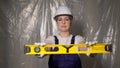 Woman builder in blue overalls and white hard hat helmet with level. Royalty Free Stock Photo