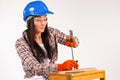 A woman builder in a helmet and goggles hammers a large nails with a hammer. White background.