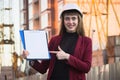 Woman builder holding blueprints, clipboard. Smiling architect girl in helmet at building background Royalty Free Stock Photo