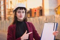 Woman builder holding blueprints, clipboard. Smiling architect girl in helmet at building background Royalty Free Stock Photo