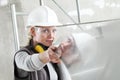 Woman builder work with the straightedge spirit level, wearing helmet, safety glasses and hearing protection headphones,