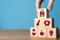 Woman building pyramid of cubes with different icons on wooden table against light blue background, closeup. Insurance concept Royalty Free Stock Photo