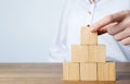 Woman building pyramid of cubes on wooden table against light background, closeup. Space for text Royalty Free Stock Photo