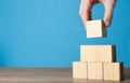 Woman building pyramid of cubes on wooden table against light blue background, closeup. Space for text Royalty Free Stock Photo