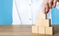 Woman building pyramid of cubes on wooden table against light blue background, closeup. Space for text Royalty Free Stock Photo