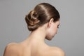 Woman with bun hairstyle on gray background. Bare back, shoulders and neck. Back view