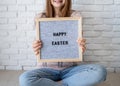 Woman in bunny ears holding felt letter board with the words Happy Easter on white brick wall background Royalty Free Stock Photo