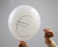 A woman bursts with a needle a balloon with the inscription euro.