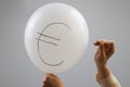 A woman bursts with a needle a balloon with the inscription euro.