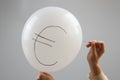 A woman bursts with a needle a balloon with the inscription euro.