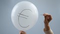 A woman bursts with a needle a balloon with the inscription euro.