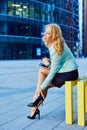 Woman in business suit and shoes sits outdoors with phone and takeaway coffee.