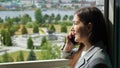 woman in a business suit is talking on the phone by the open window against the background of a green park Royalty Free Stock Photo