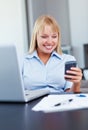 Woman busy on her cell phone. Happy young business woman reading text message with laptop on desk. Royalty Free Stock Photo