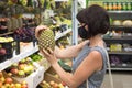 Woman buyer in a protective medical mask chooses a pineapple