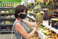 Woman buyer in a protective medical mask chooses a pineapple